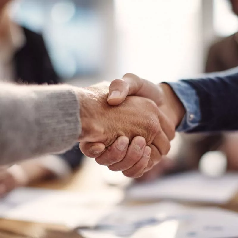 Close-up of two people shaking hands over a table